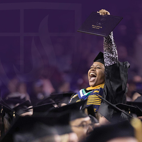 A student holding up their diploma at graduation