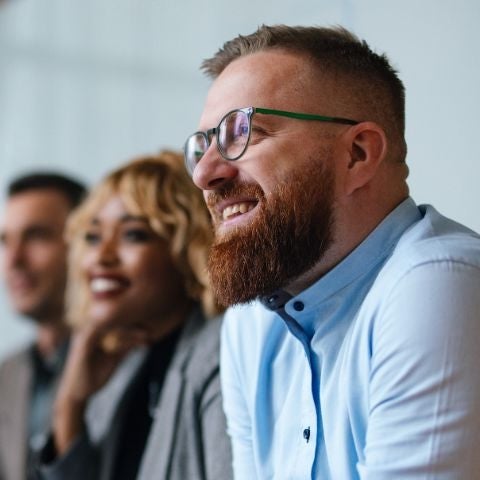 Smiling businessman and employees sitting in a row at their company desk and listening to their boss.