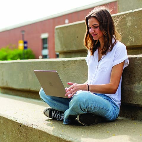 A woman sitting on steps outside working on a laptop