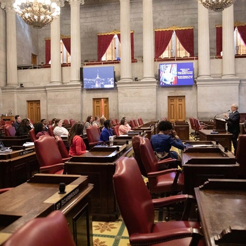 Students seated in the Tennessee House of Representatives chamber listening to a speaker at a podium.