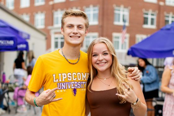 Two students at event making horns up hand gesture.