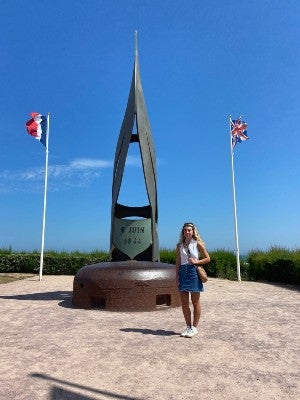 Kaela Abbate posing next to a memorial statue on Normandy Beach