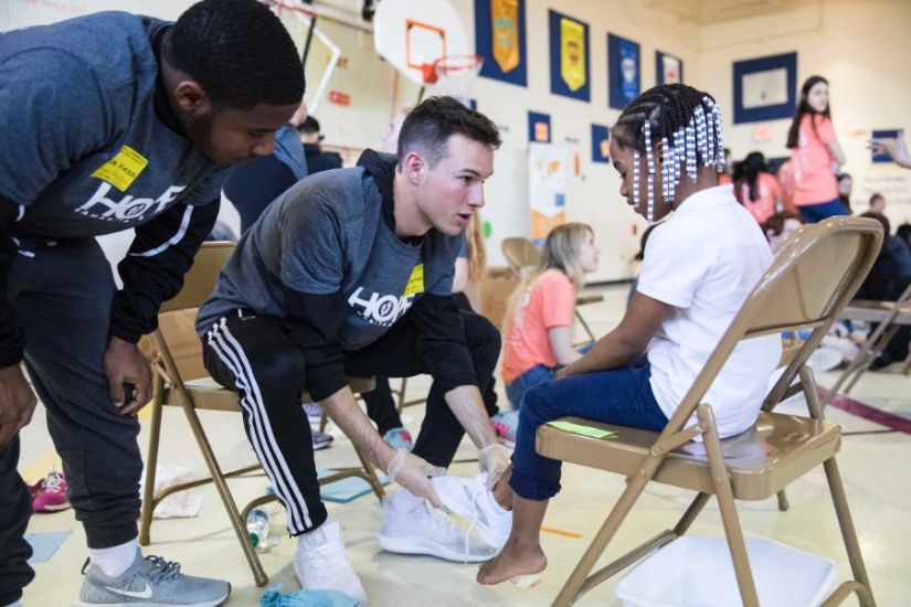 Students help an elementary schooler find the perfect pair of shoes