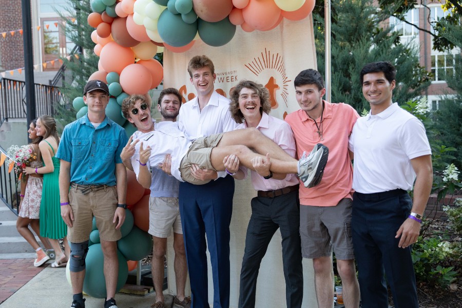 Male students pose in front of banner at Sunset Social