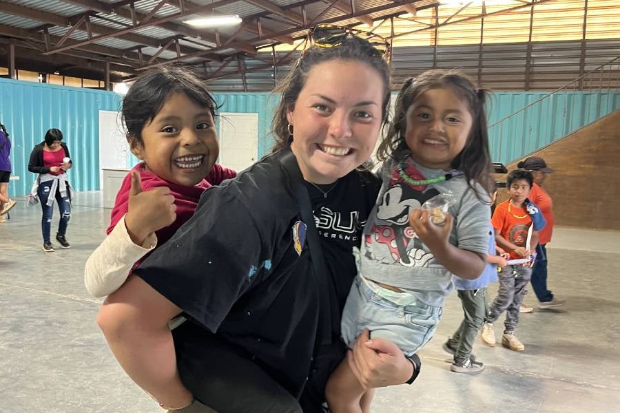 Elise Shewmaker holding two small children during mission trip.