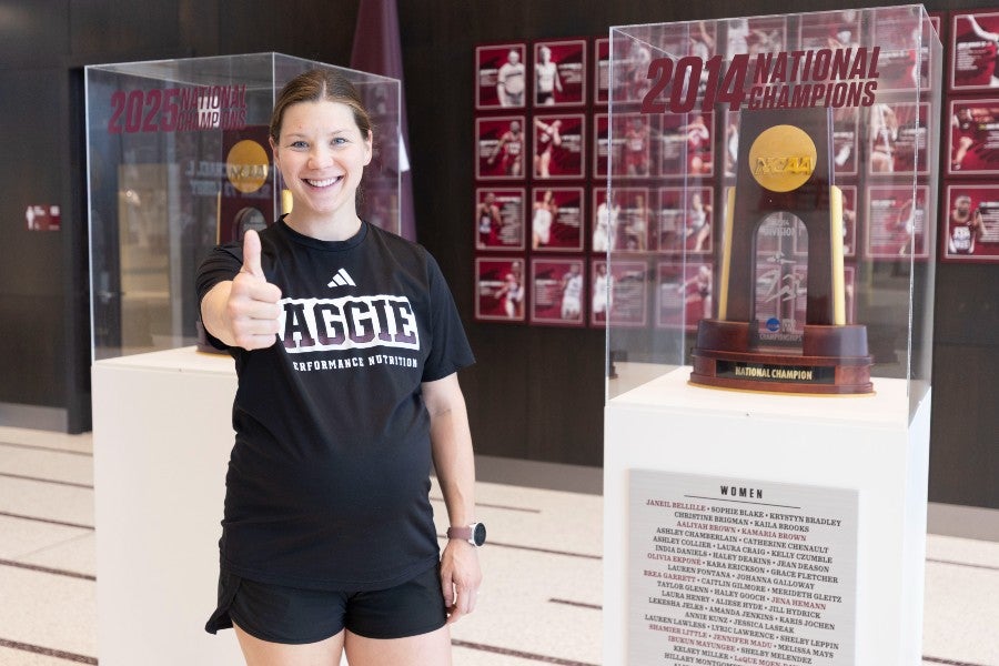 Margo Newman posing in front of the Texas A&M tennis team championship  trophy
