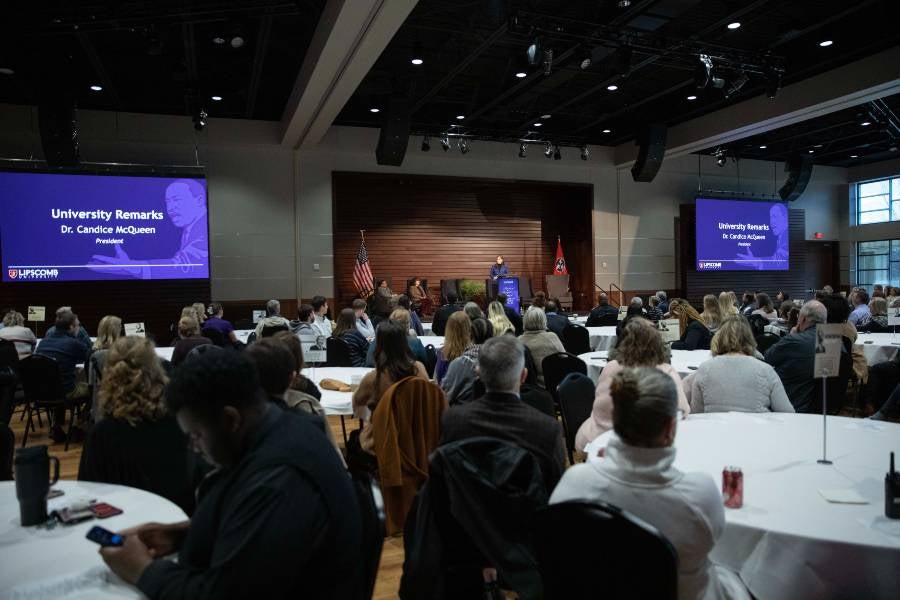 Faculty and staff sitting at tables inside the George Shinn Center listening to Dr. Candice McQueen speaking. 