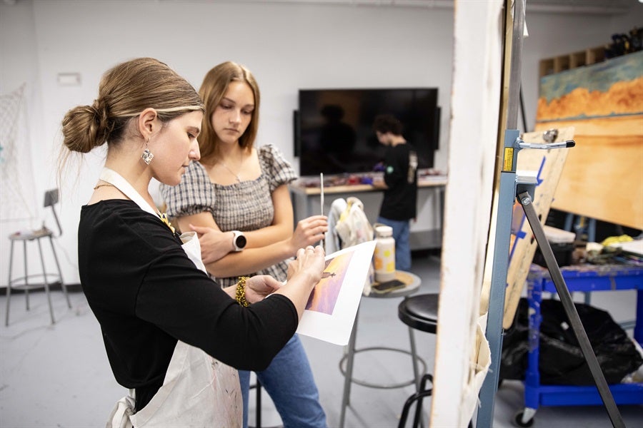 a student paints and a teacher watches