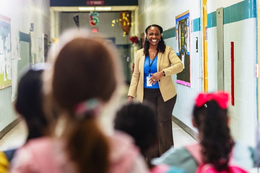 A principal greeting school children in a school hallway