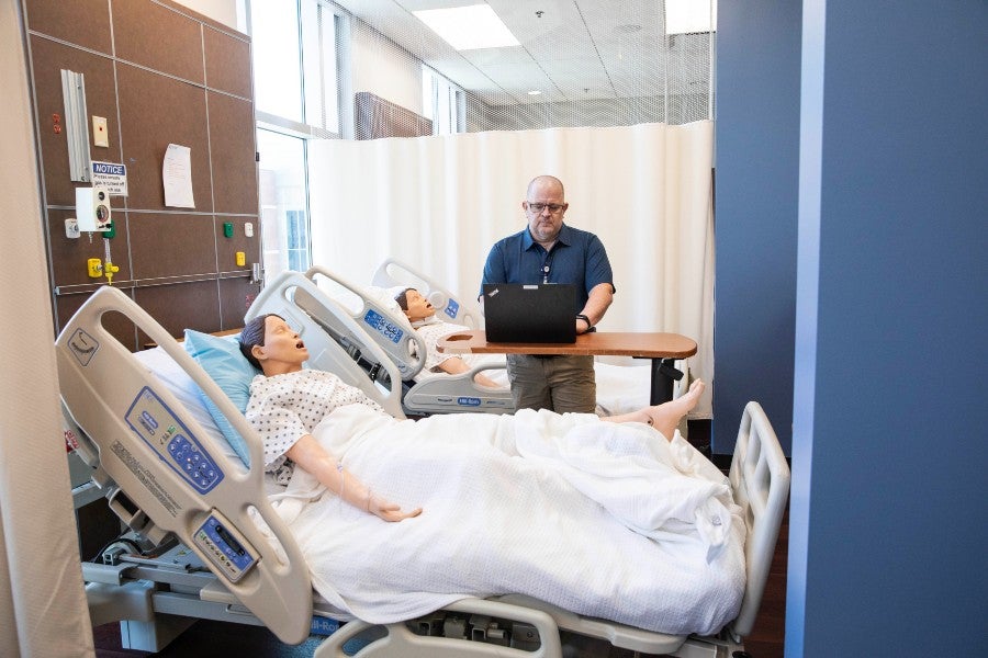 Jeffrey Adams working with a laptop at the bedside of a patient simulator