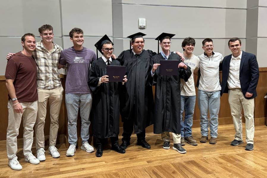 Group of students standing with several graduates. 