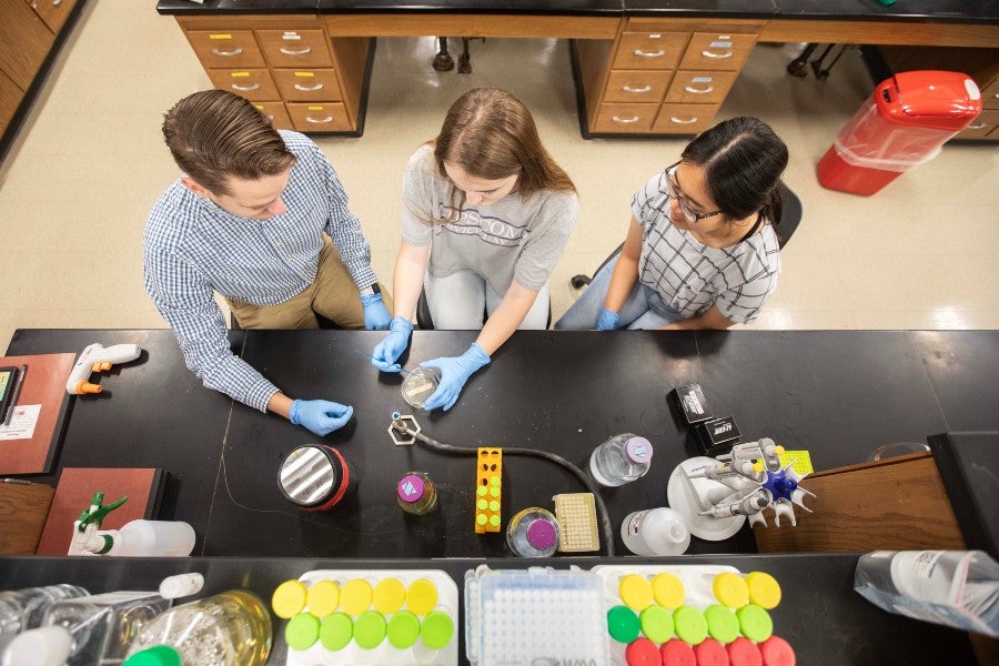 Josh Owens working with two students in the biology lab
