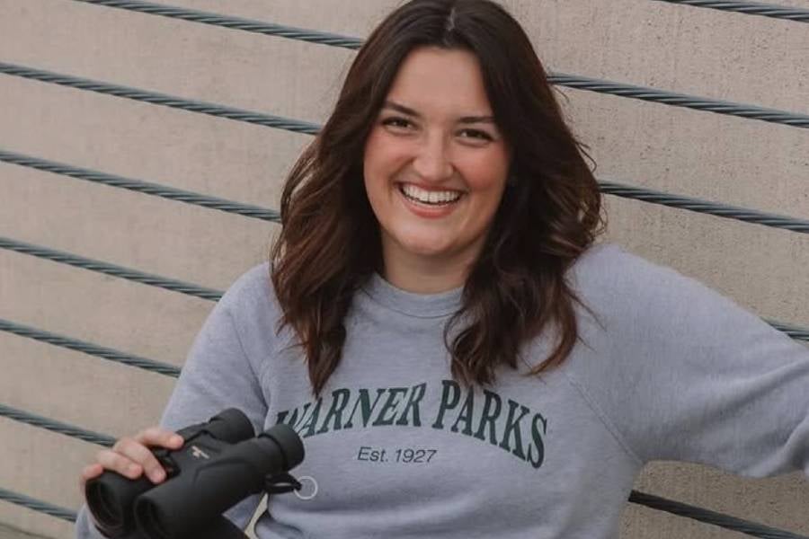 Lexi Price sitting outside wearing a Warner Parks sweatshirt and holding binoculars. 