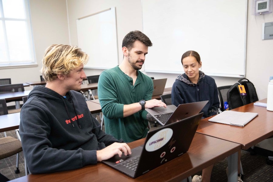 Zach Droll (center) working with students at their laptops in class