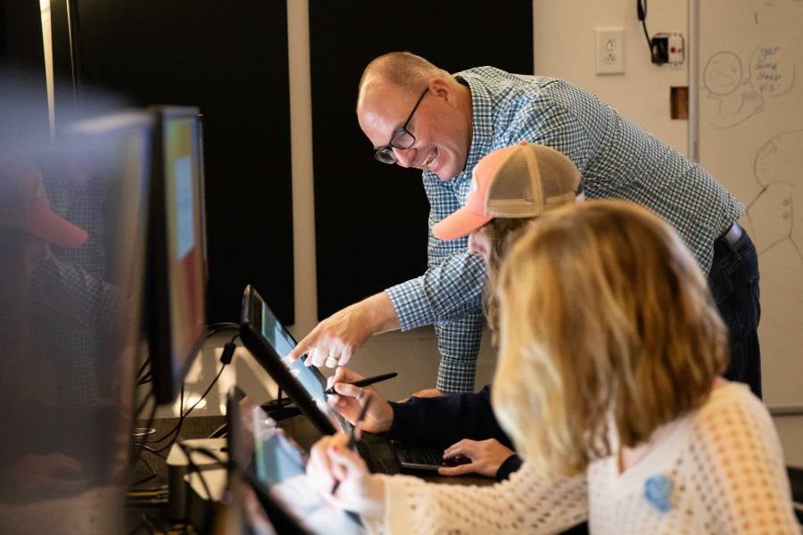 Tony Bancroft in a class looking at a computer screen with students. 