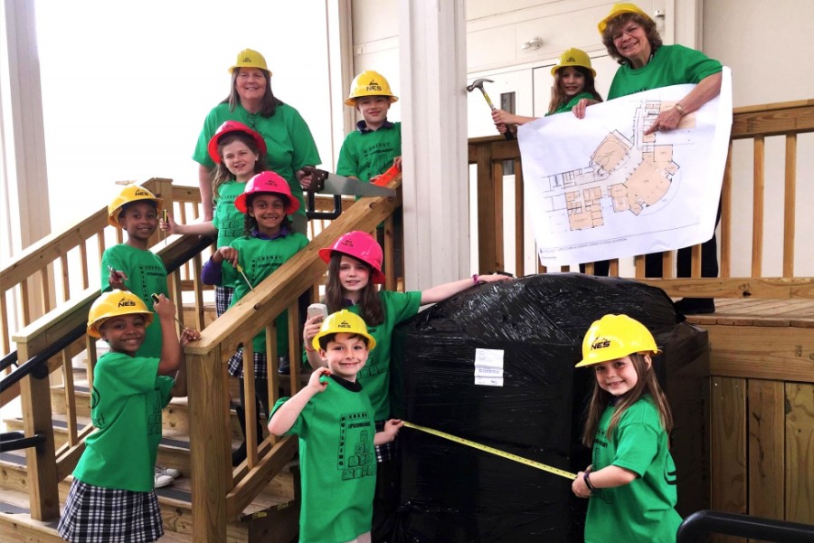 Elementary school children standing outside wearing hard hats. 