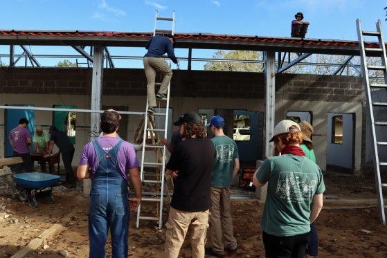 Students helping work on the roof of a covering and climbing a ladder.