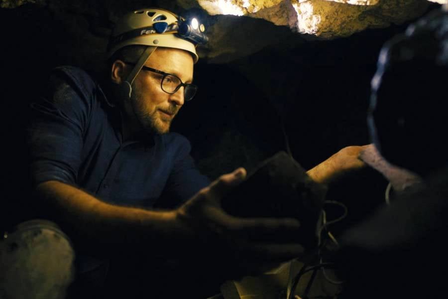 Lipscomb professor Chris McKinny on an excavation site wearing a hard hat and head lamp in a scene from the film. 