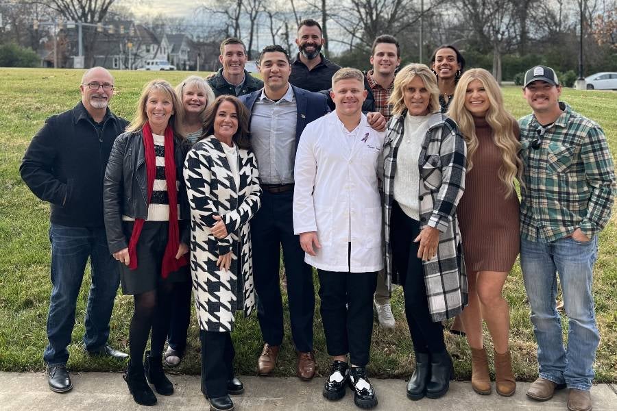 Trever Facey, in white coat, surrounded by family and friends at nursing pinning ceremony. 