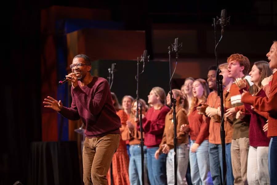 Gospel Choir director Aaron Howard singing on stage with members of the Gospel Choir standing behind him. 