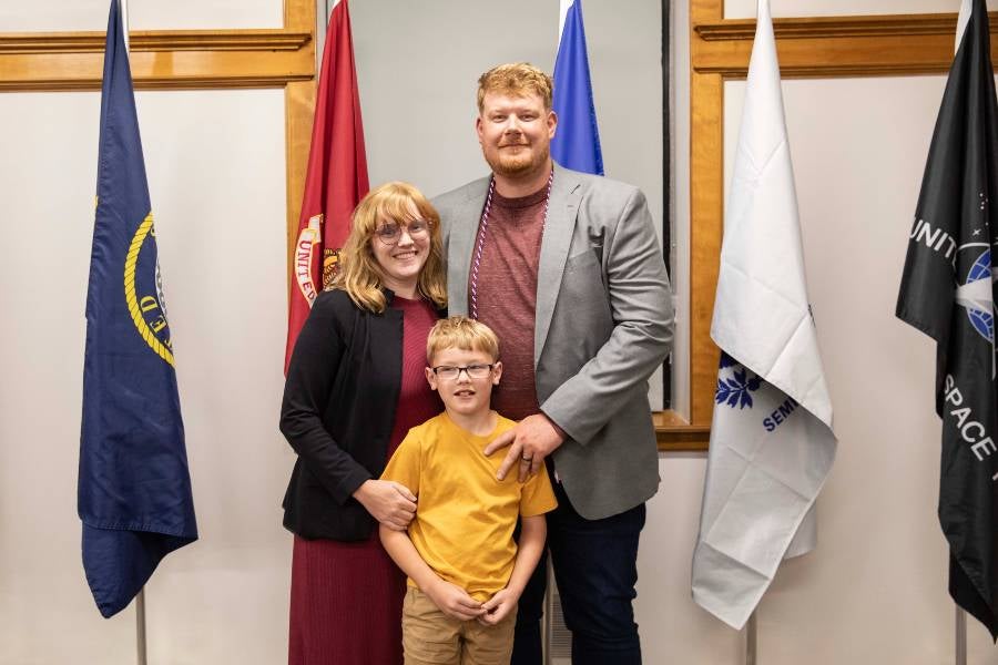 Lucas Landis with his wife and one of their three children standing by flags. 
