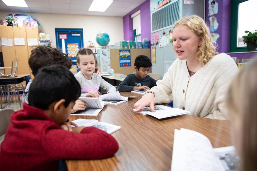Teacher sitting at desk with students reading. 