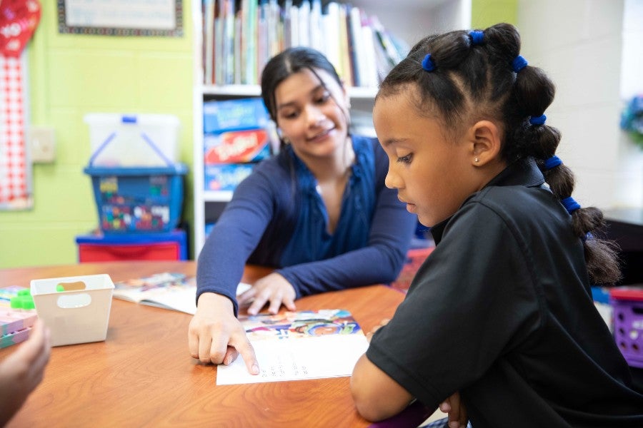 Teacher sitting at desk with students reading. 