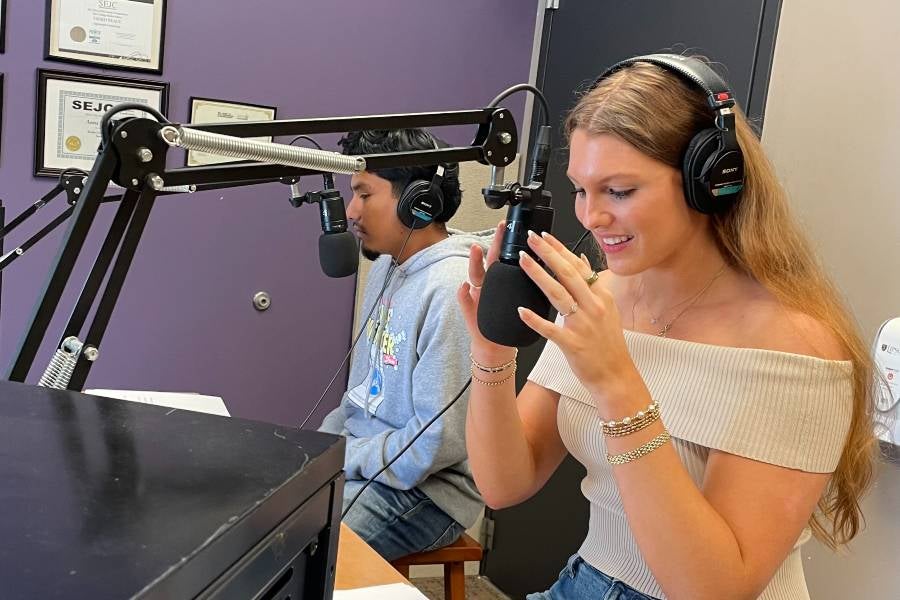 Samuel Espinoza and Olivia DeRocher anchor the award-winning newscast for The Bison. They are sitting in the sound booth wearing headphones.