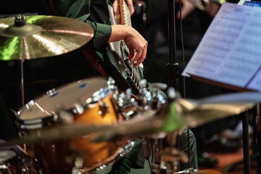 a musician playing guitar as seen through a drum set