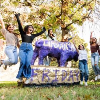 Students jumping in excitement in front of the Bison Statue