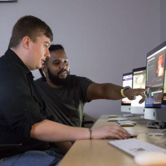 two men looking at a desktop computer and researching
