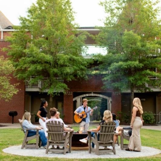 Students around a campfire listening to guitar