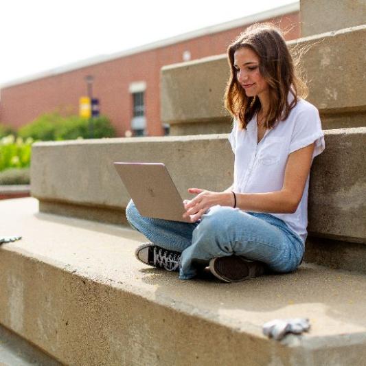 A woman sitting outside on steps and working on her laptop