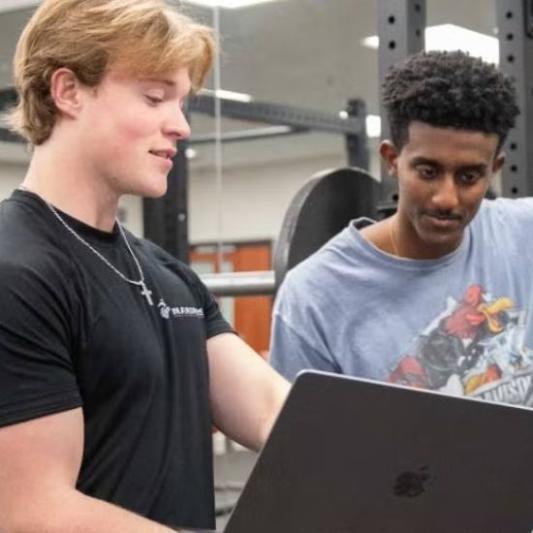 Students in a gym looking at data on a laptop
