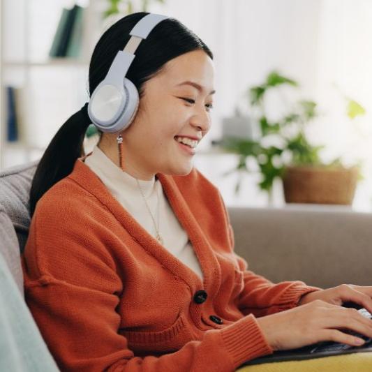 A girl with headphones on smiling and working on her computer.