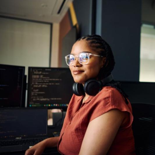 Girl with headphones facing the camera sitting at her computer