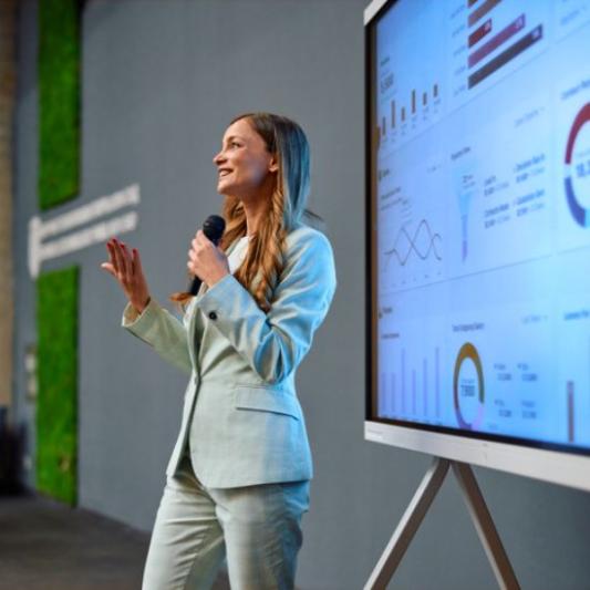 Woman at work standing with a microphone and giving a presentation.