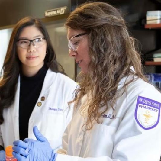 Two women in a lab wearing lab coats and working with a beaker