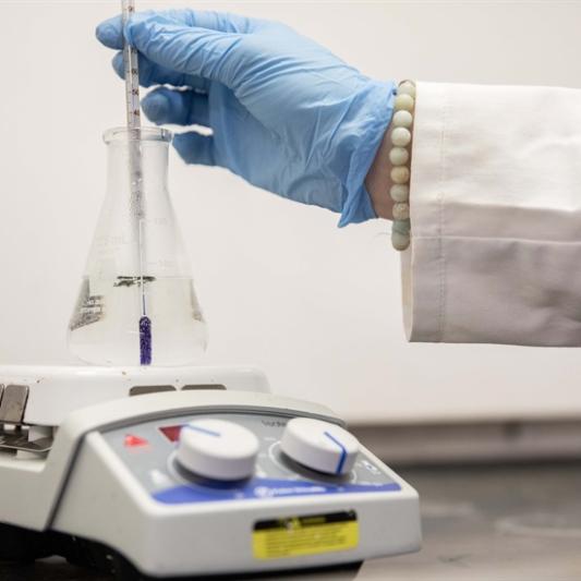 a gloved hand places a beaker on a measurement instrument