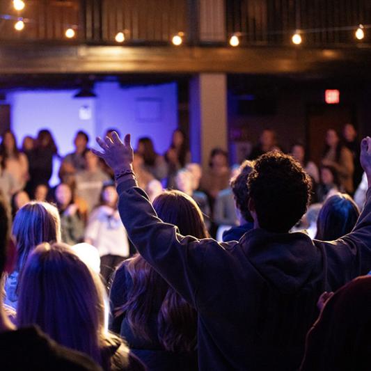 Students in a worship service lifting hands. 