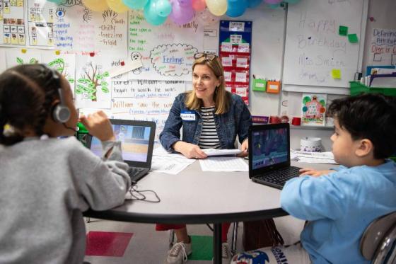 Teacher sitting at a table working with two elementary school aged students. 