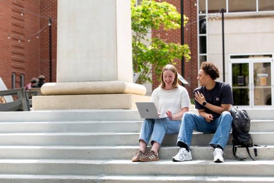 Two students sitting on the steps of Beaman Library looking at a computer. 