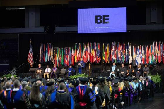 the stage at Convocation with university leaders seated in front of a row of flags