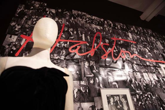 Mannequin wearing a Halston outfit in front of a backdrop of Halston photographs